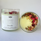 Candle labeled 'Light of Soul Apothecary Hecate' with dried flowers on a white background