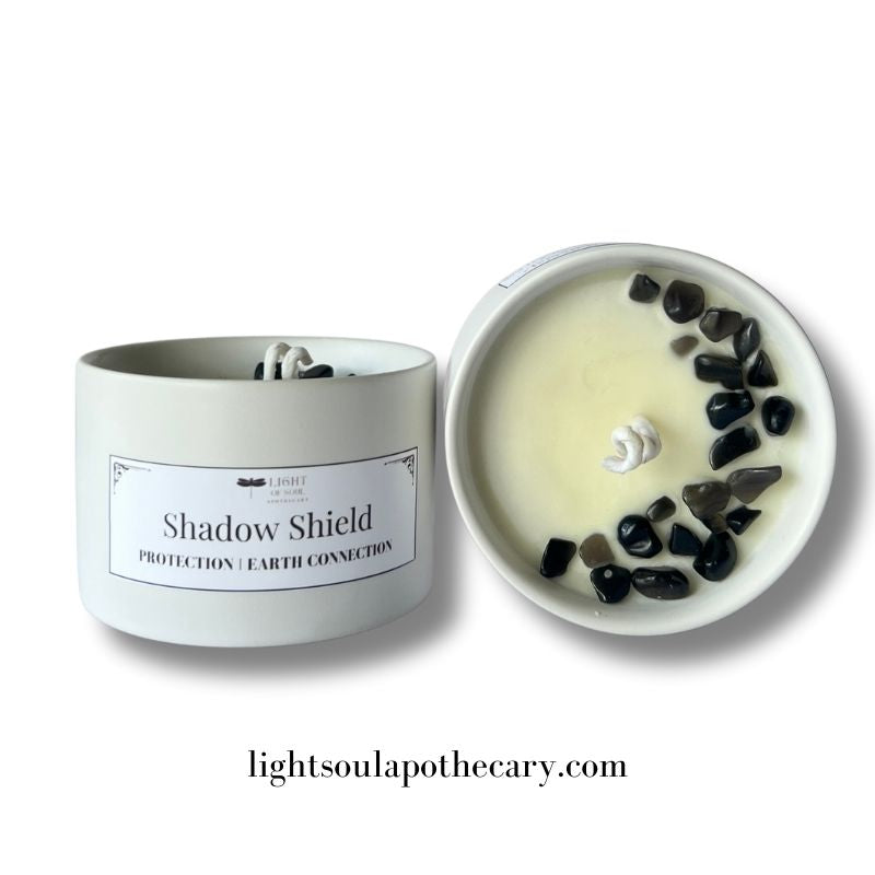 Candle labeled 'Shadow Shield' with pebbles on a white background